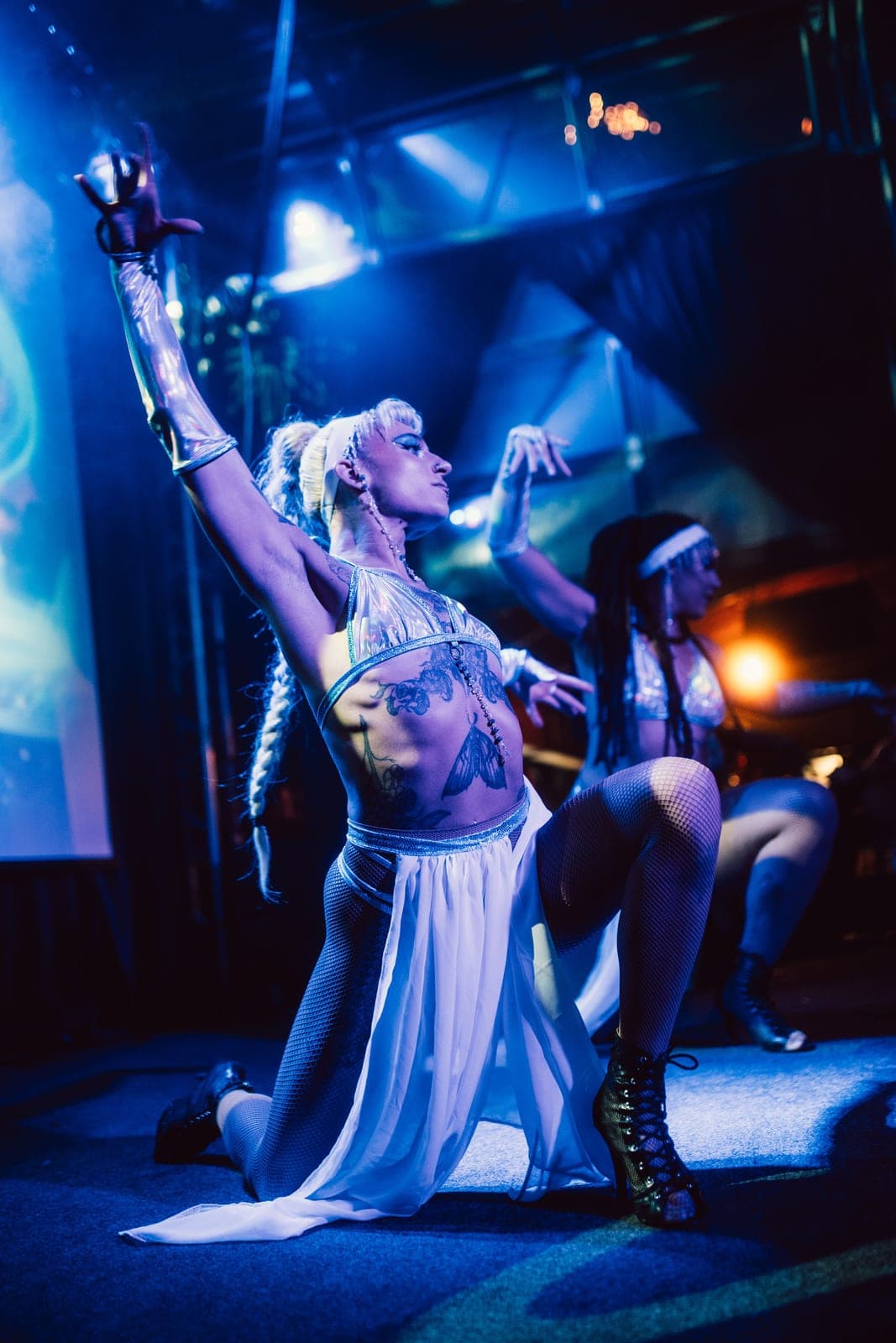 Three Levity Arts performers on stage together in costume, lit in blue
