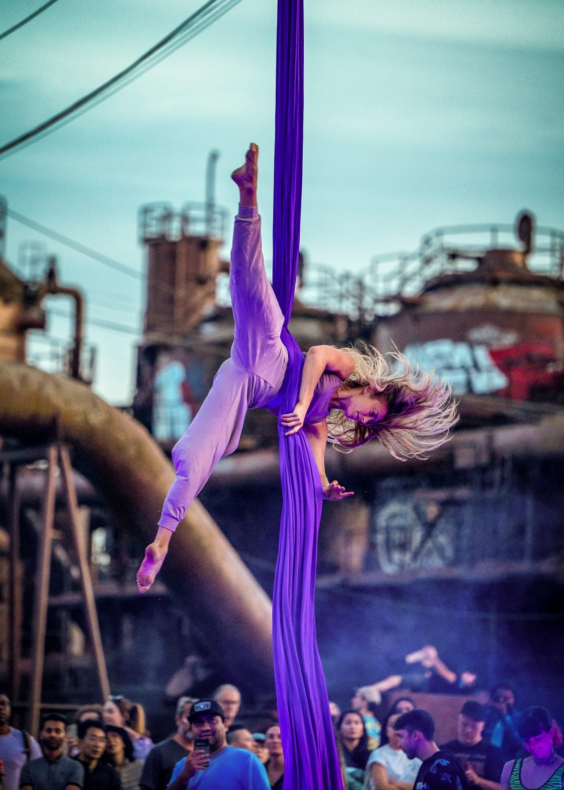 An aerialist on purple silks at Gas Works Park, industrial towers behind