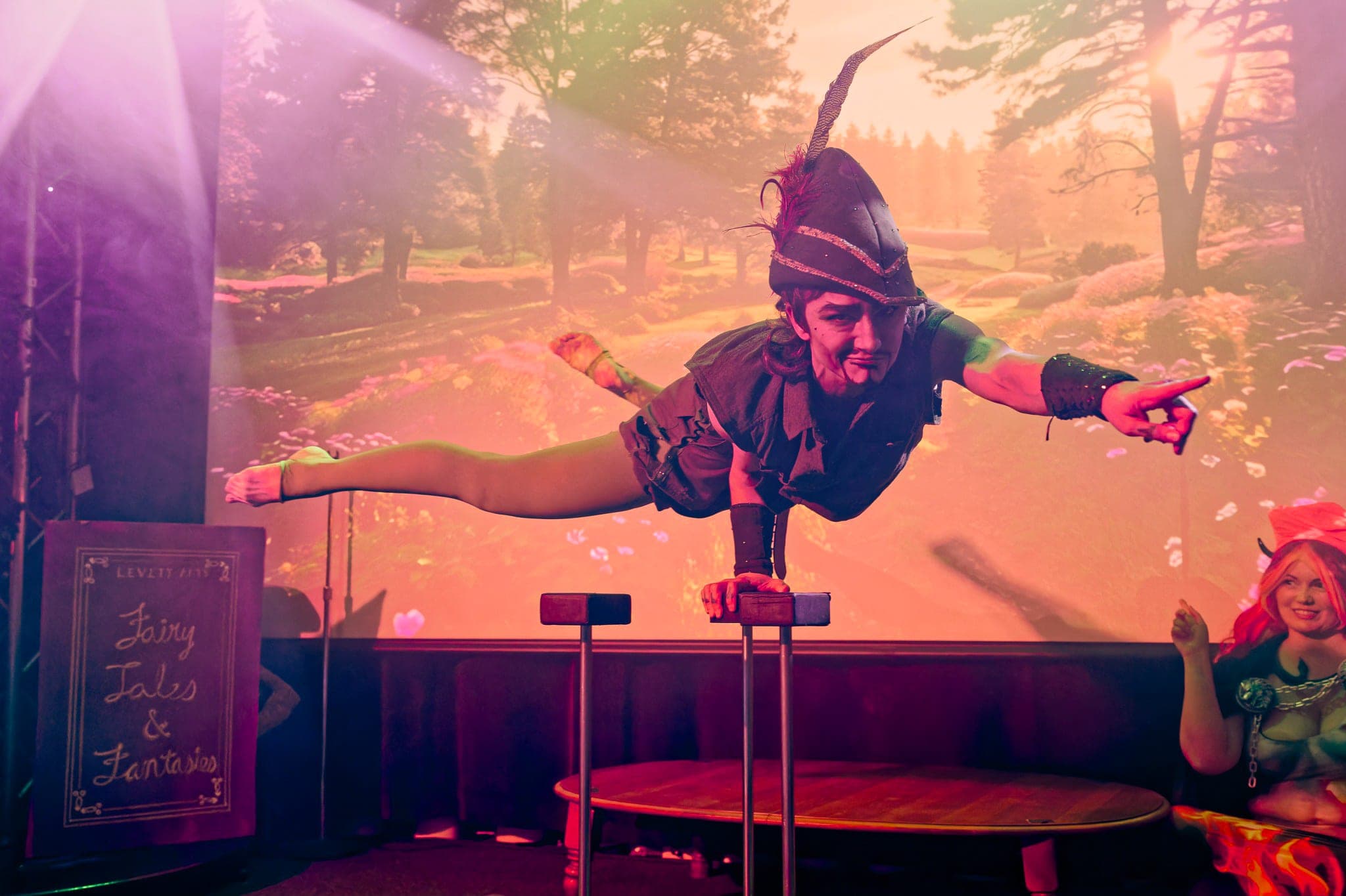 A performer balancing on canes in front of a projected forest backdrop