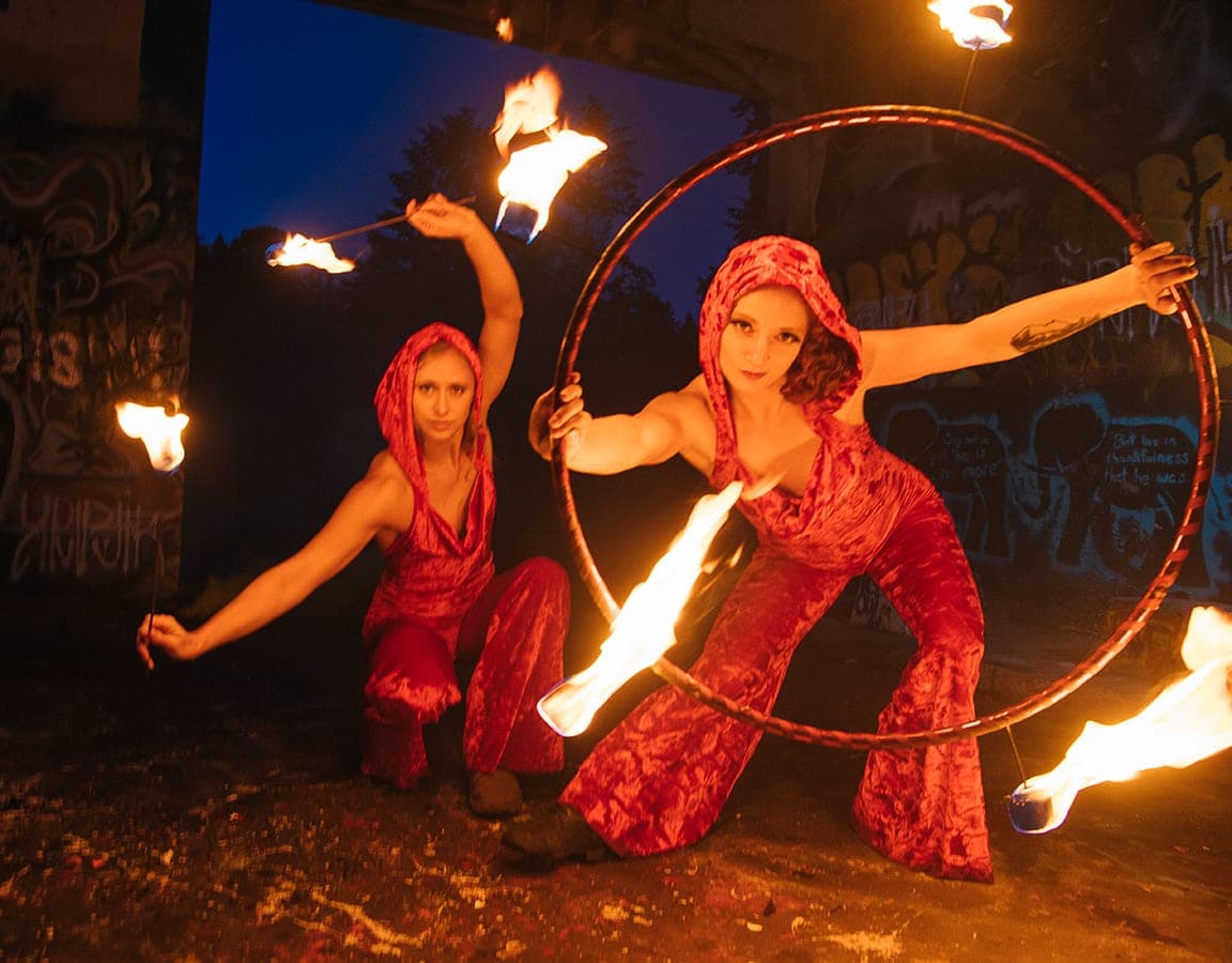 Two fire performers with a flaming hoop against a graffiti wall at night