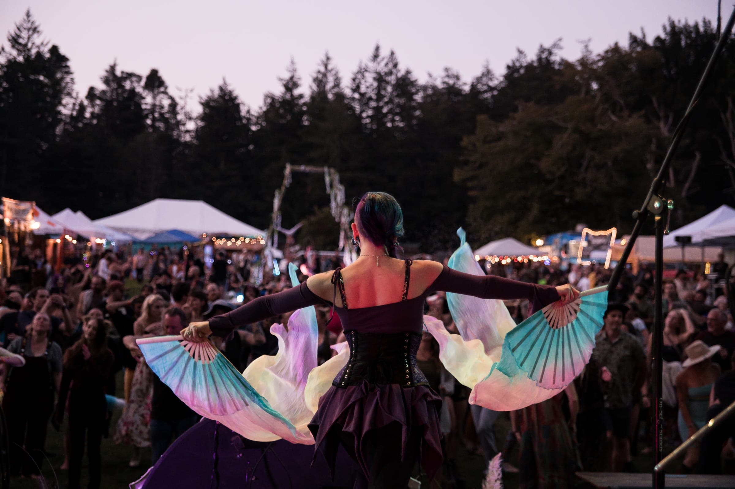 A performer with feathered fans facing a large outdoor crowd at dusk