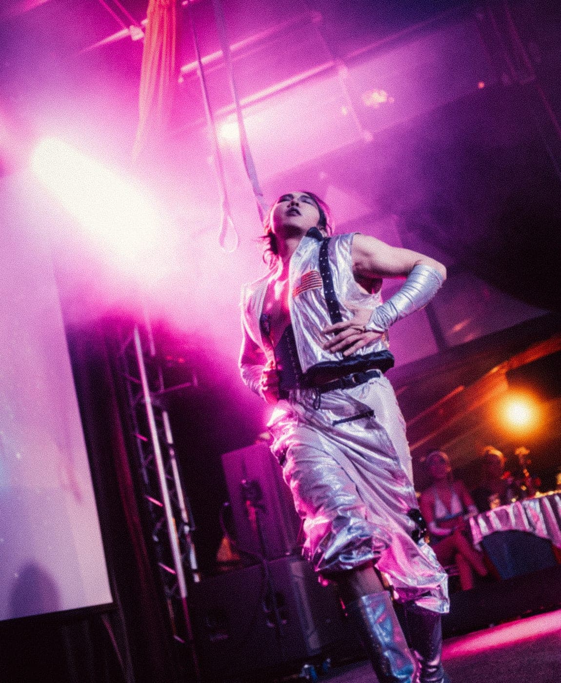 A performer in silver mid-routine under pink stage light