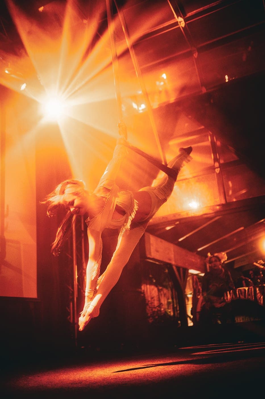 An aerialist suspended in a beam of warm spotlight