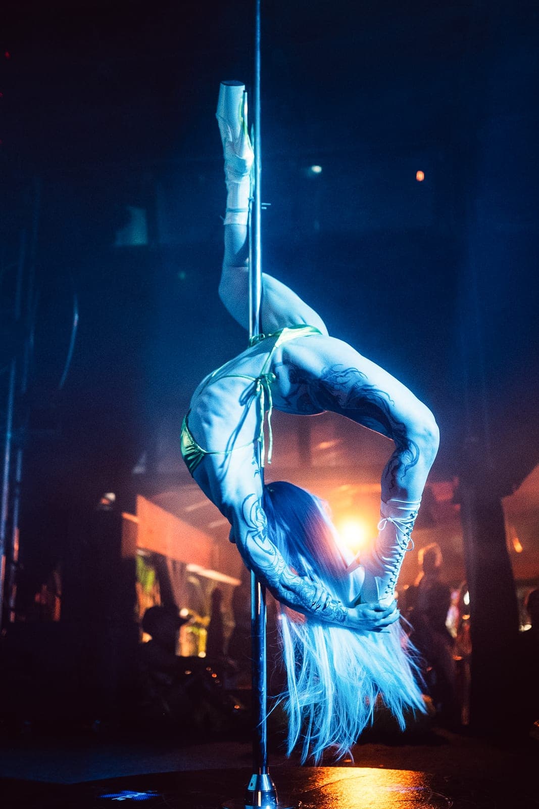 A pole performer in a deep backbend, lit in blue