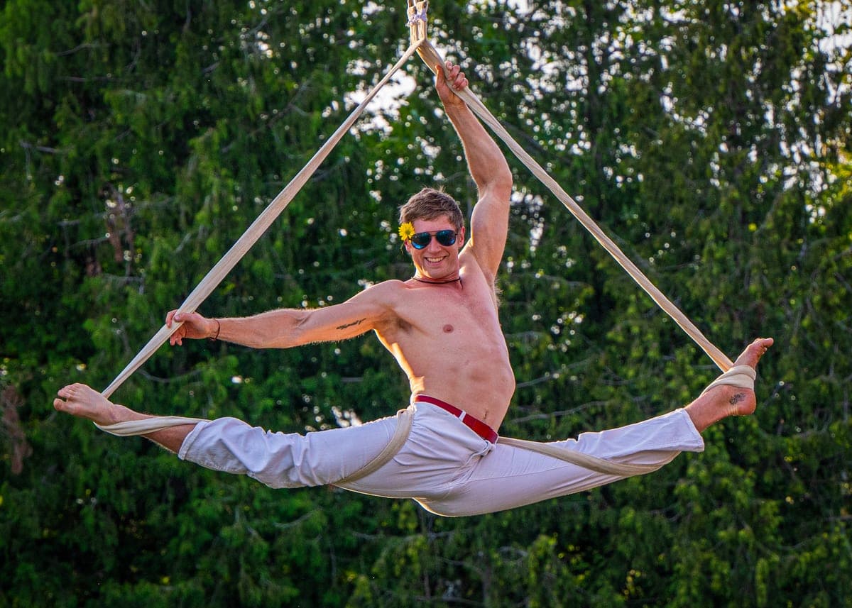An aerialist holding a split on a frame apparatus among summer trees