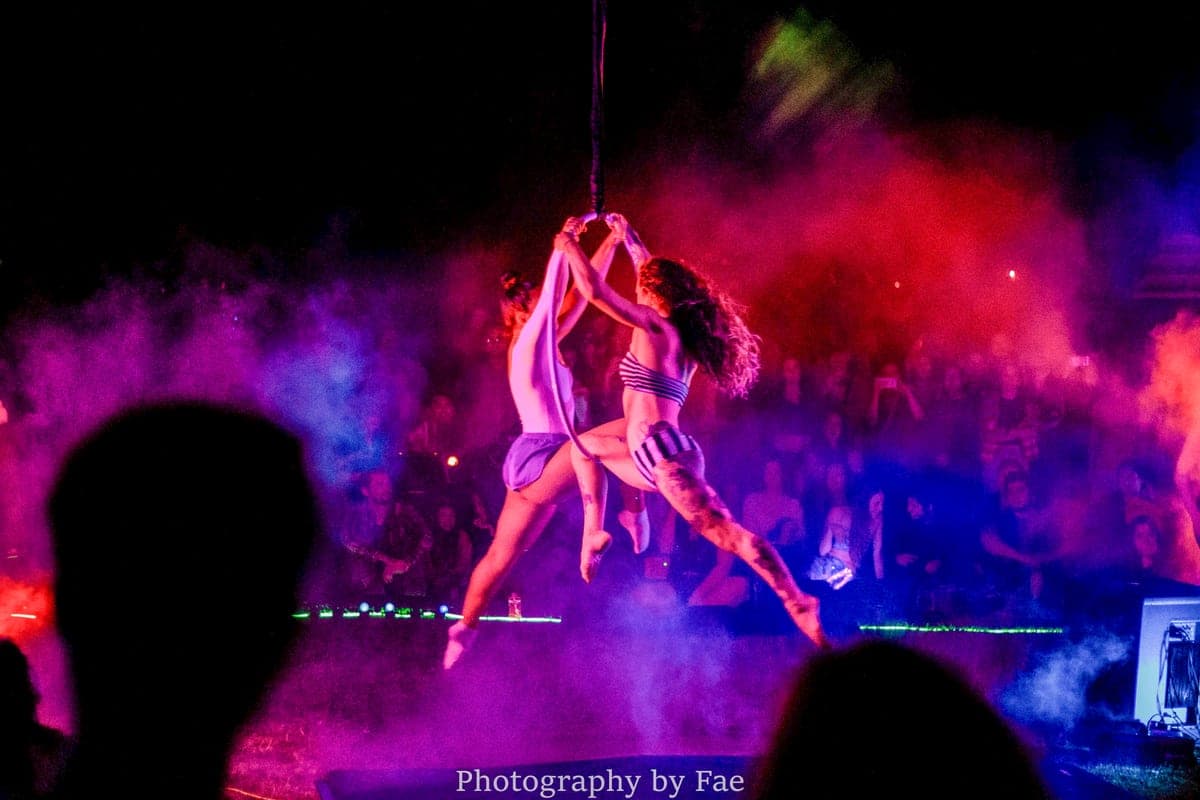 Two aerialists on a hoop in clouds of pink and purple smoke above a crowd