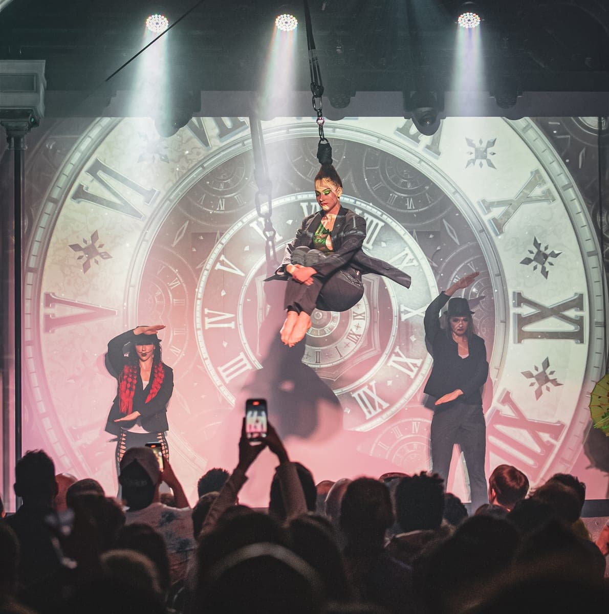 An artist suspended by their hair in front of a giant clock projection