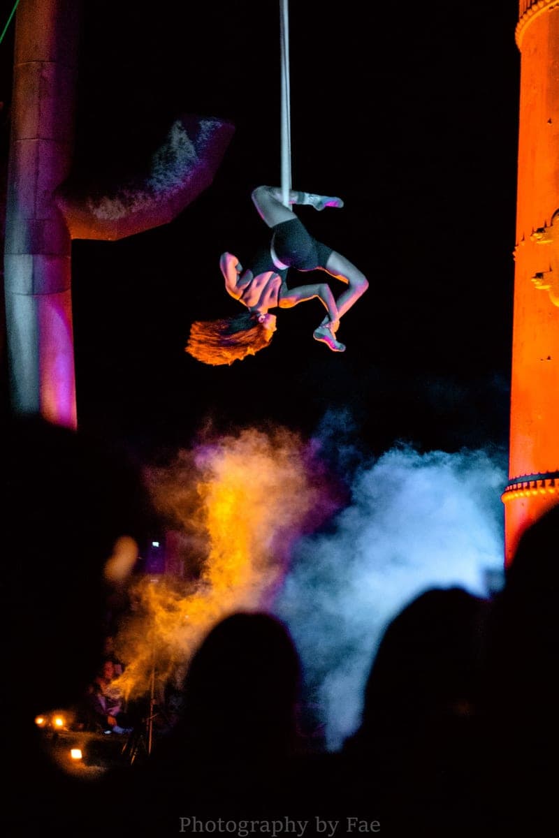 An aerialist lit by fire and smoke at a night-time performance